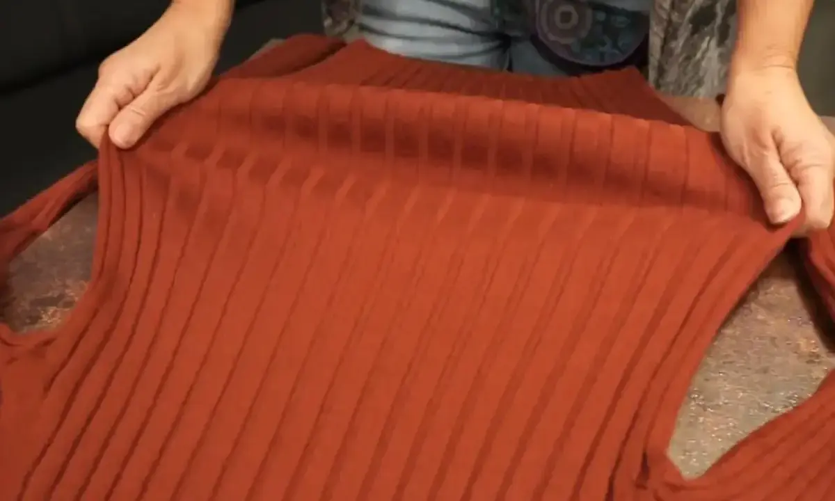Hände halten einen verfilzten und eingelaufenen Pullover aus Rippstrick. Essig als Hausmittel zur Rettung?