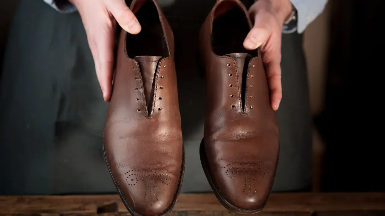 Hände präsentieren braune Lederschuhe, bereit für die Fettleder Pflege.