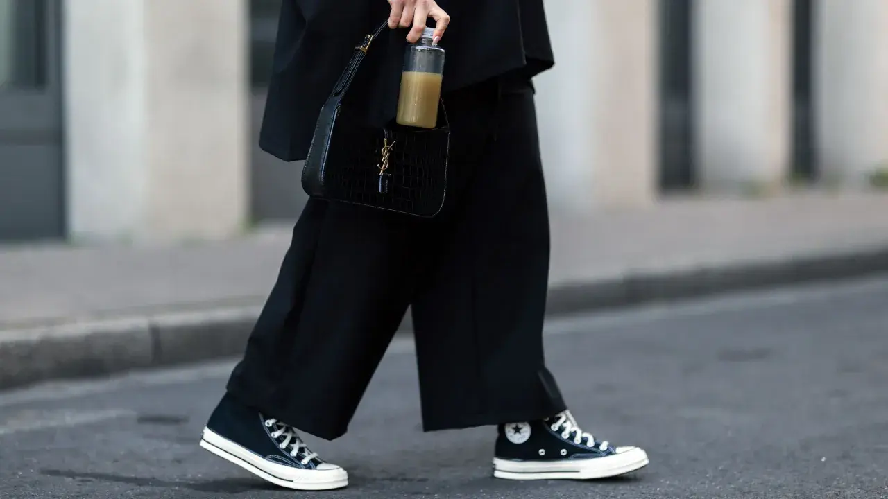 Schwarze, weite Hose und hohe Chucks kombinieren Damen für einen lässigen Look. Dazu eine schwarze Kroko-Tasche und eine Wasserflasche.