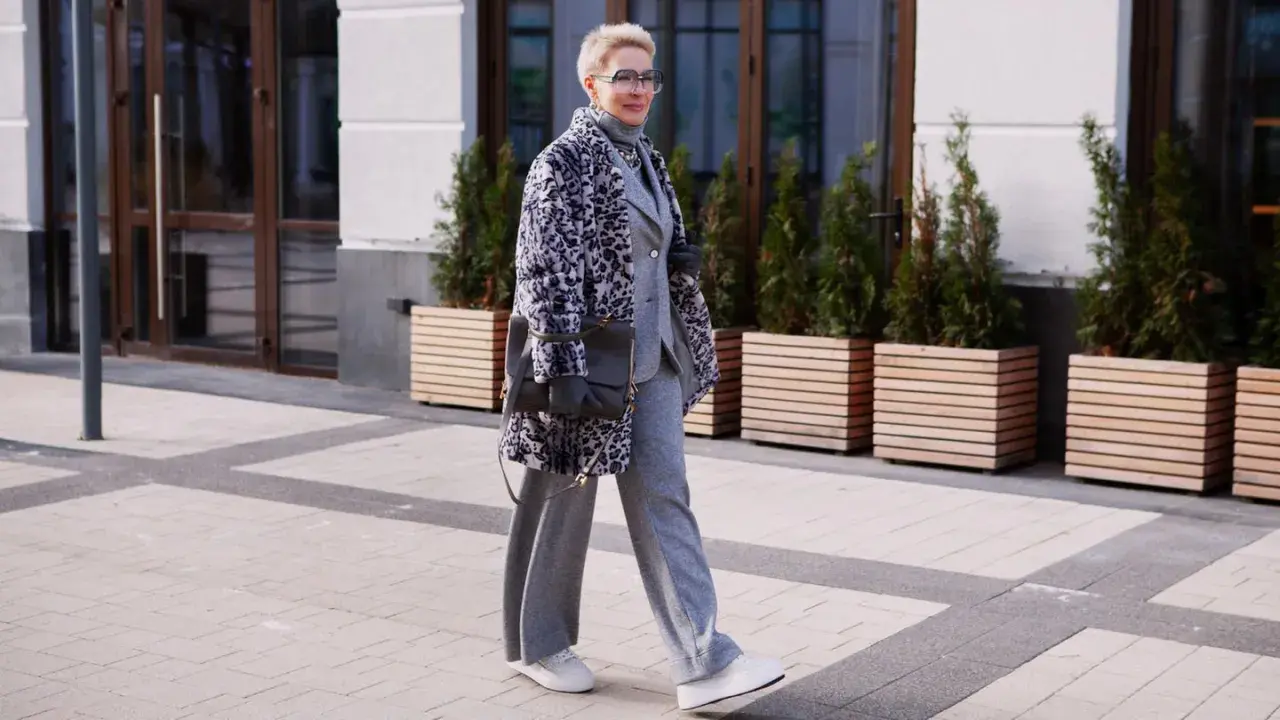 Stilvolle Frau in grauem Anzug und Strickhose, kombiniert mit einem gemusterten Mantel und Sneakern.