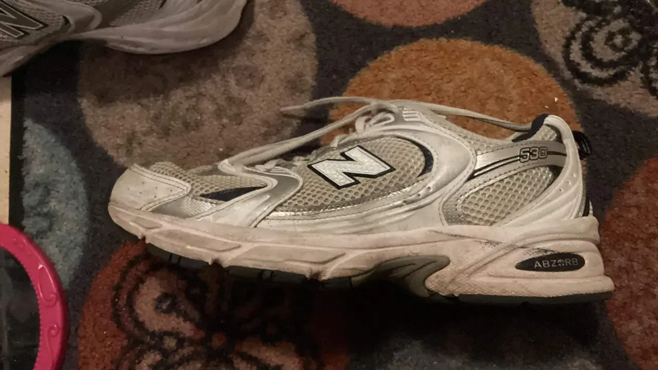 Ein schmutziger New Balance 530 Sneaker liegt auf einem gemusterten Teppich. Zeit, ihn zu waschen!