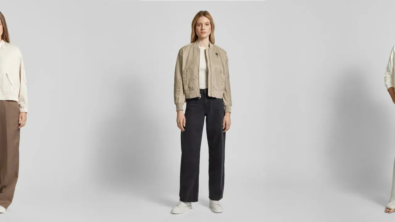 Drei Frauen präsentieren lässige Outfits. Die mittlere Frau zeigt, wie man eine Bomberjacke stylen kann, kombiniert mit weiten Jeans und Sneakern.