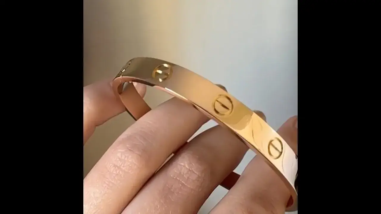 Vergleich: Fake Cartier Love Armband vs. echt. Ein glänzendes, roségoldenes Armband mit Schraubenmotiv wird von Fingern gehalten.