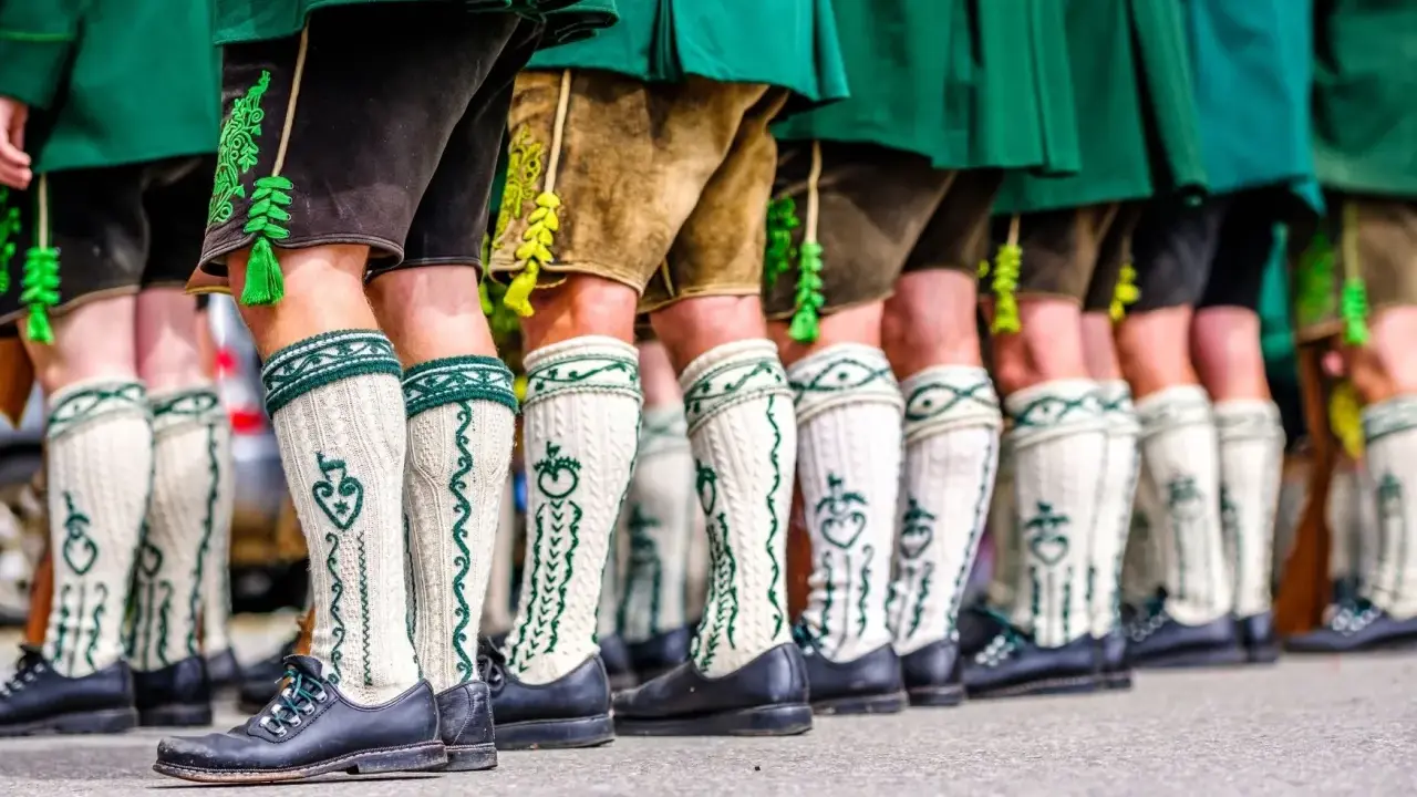 Herren in Lederhosen und traditionellen Strümpfen tragen passende Schuhe. Welche Schuhe zur Lederhose Herren? Schwarze Trachtenschuhe sind hier die Wahl.