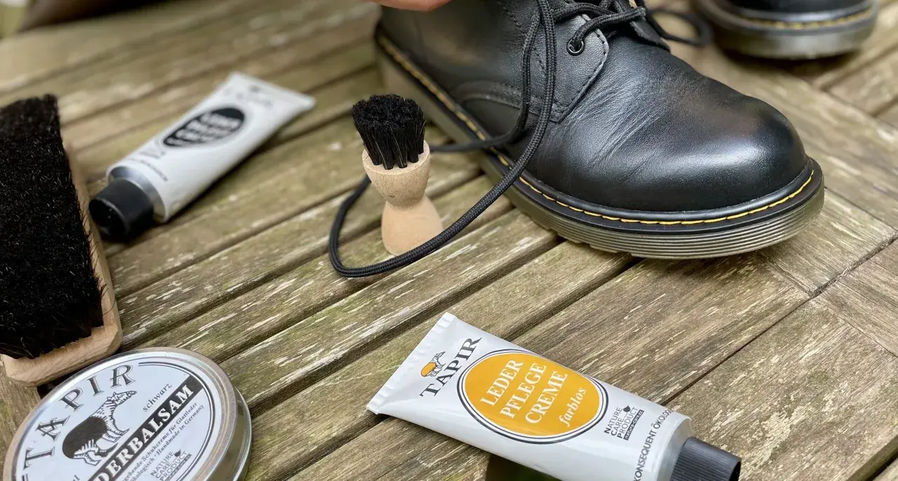 Schwarze Lederstiefel werden mit Tapir Lederpflegecreme und Bürsten gepflegt.
