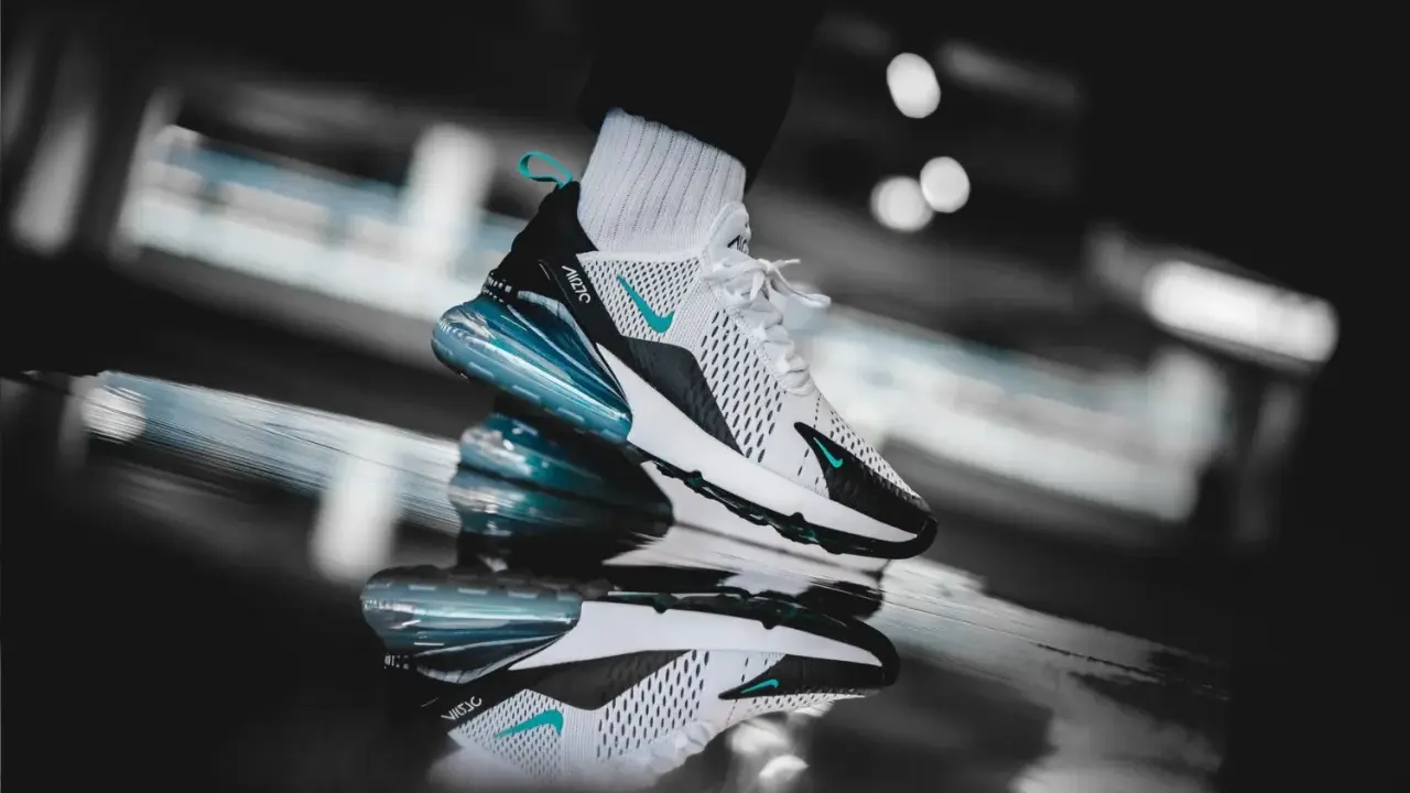Ein stylischer Nike Air Max 270 in Weiß mit türkisen Akzenten, der auf einer spiegelnden Oberfläche steht. Ein zeitloser Klassiker unter den Nike Air Max alte Modelle.