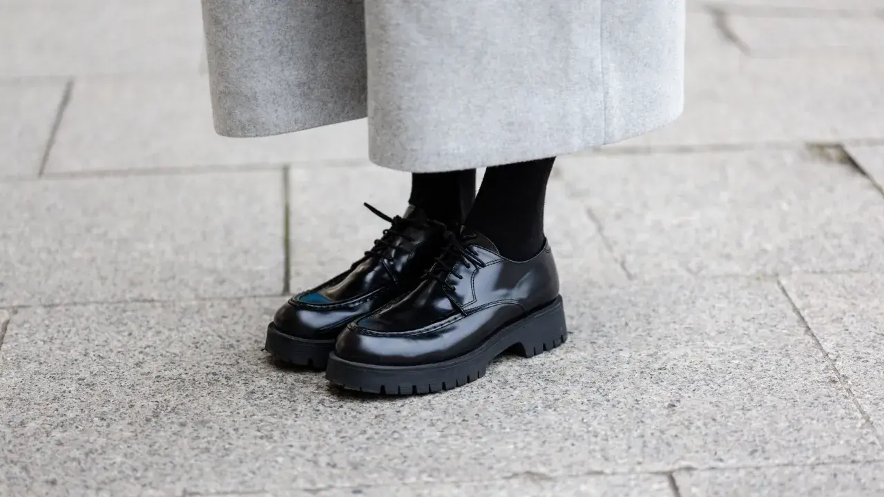 Schwarze Schnürschuhe mit dicker Sohle, ein moderner Schuh-Typ für Damen, kombiniert mit einem grauen Wollrock.
