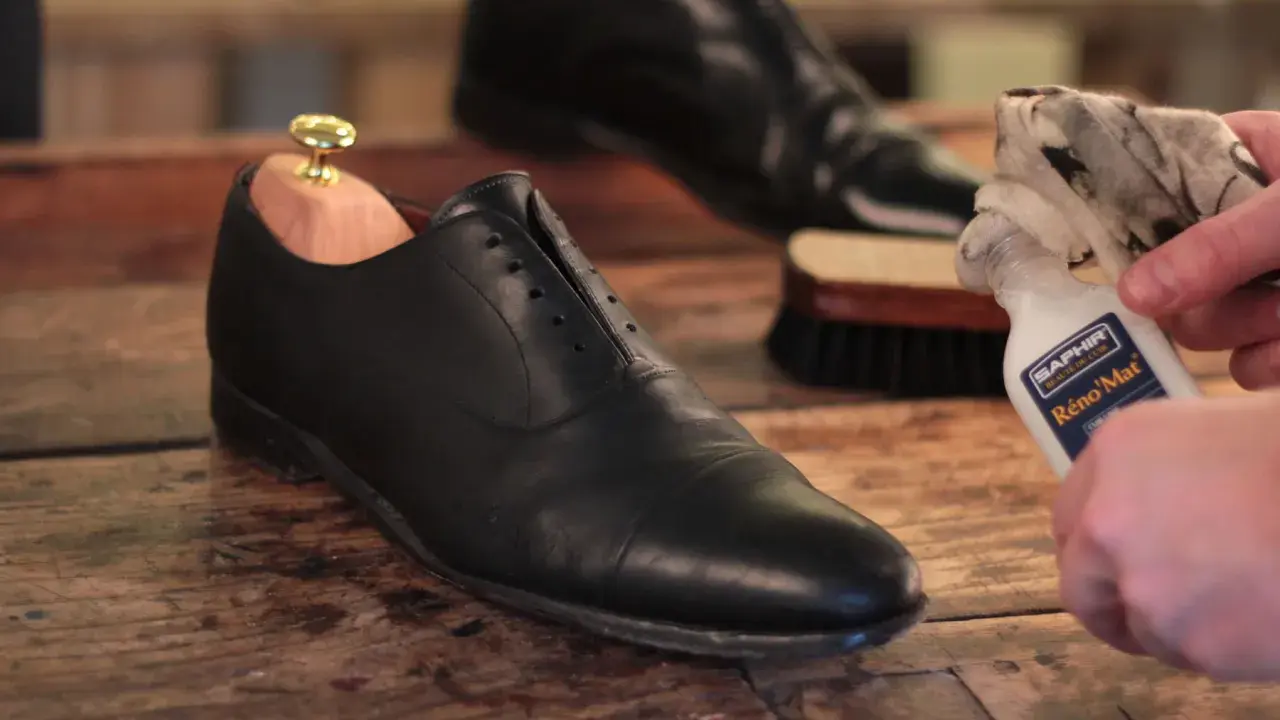 Schuhe polieren: Ein schwarzer Lederschuh mit Schuhspanner wird mit einem Tuch und Saphir Reno'Mat gereinigt.
