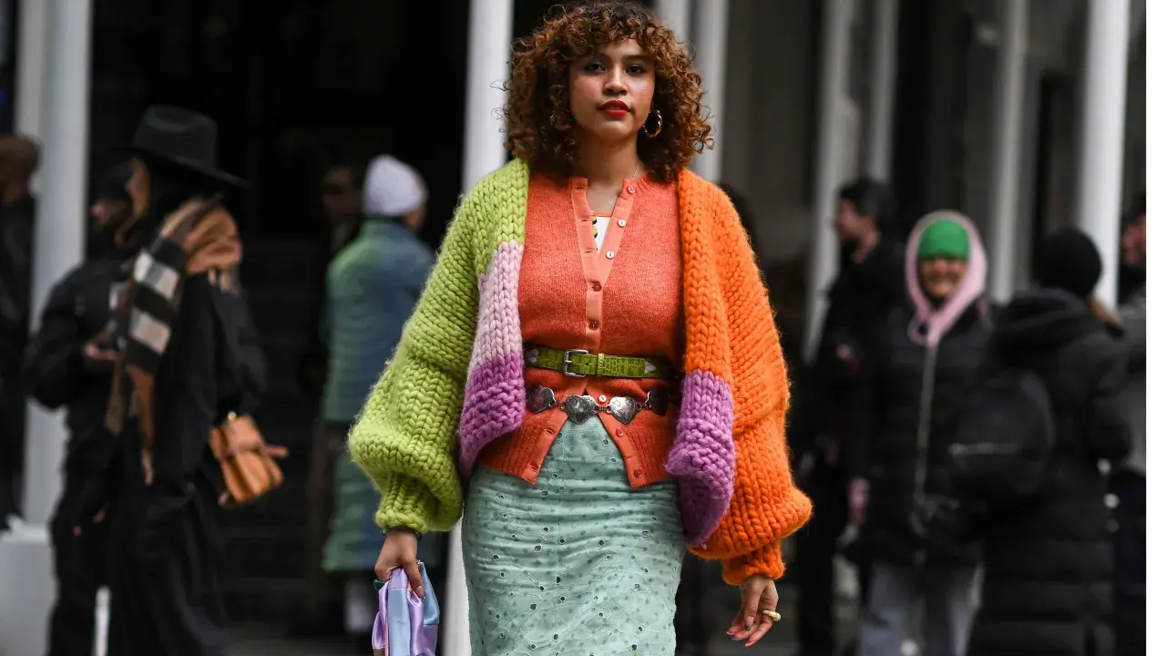 Bunte Strickjacke mit Ballonärmeln, die zeigt, wie man einen Cardigan kombinieren Damen kann. Dazu ein mintgrüner Rock und auffälliger Gürtel.