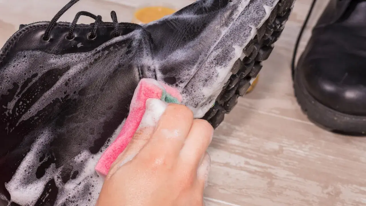 Schwarze Lederschuhe werden mit einem Schwamm und Seifenschaum gereinigt. Die Sohle und das Leder werden sorgfältig abgerieben, um sie wieder sauber zu machen.