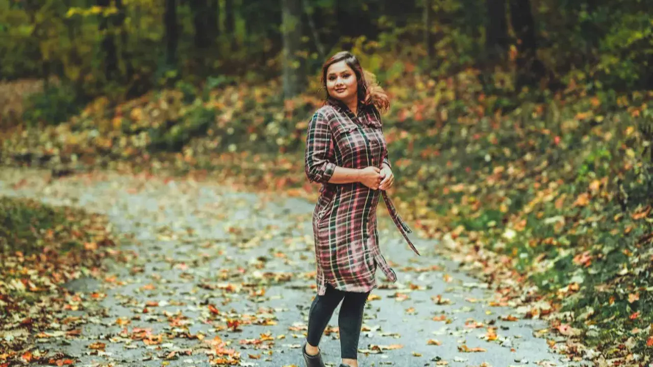 Frau im karierten Kleid mit Leggings steht auf einem herbstlich bedeckten Weg.
