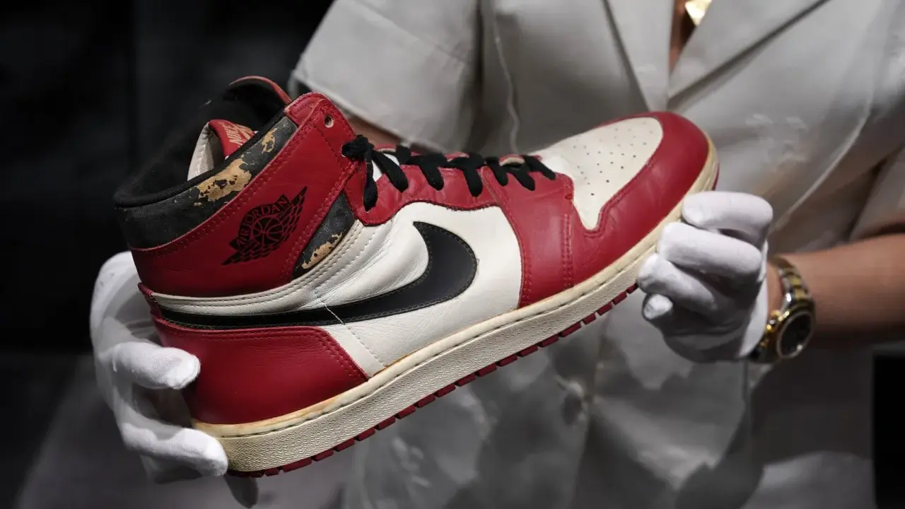 Ein Paar rote und weiße Air Jordan 1 Sneaker, die als die teuersten Schuhe der Welt gelten, werden von Händen in weißen Handschuhen gehalten.