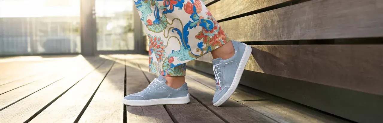 Blaue Wildlederschuhe mit weißer Sohle und dezenter Ziernaht am Schuh, kombiniert mit einer Hose mit floralem Muster.