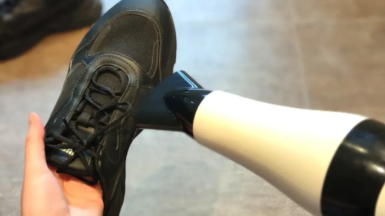Schwarze Turnschuhe trocknen mit einem Föhn.