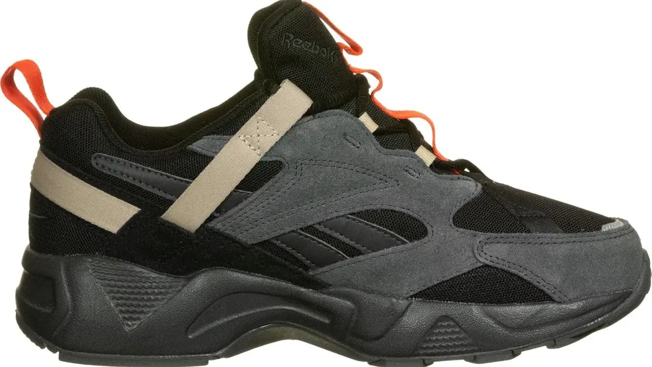 Reebok Aztrek 96: schwarzer Sneaker mit grauen Wildleder-Overlays, beige Akzenten und orangefarbenen Schlaufen.
