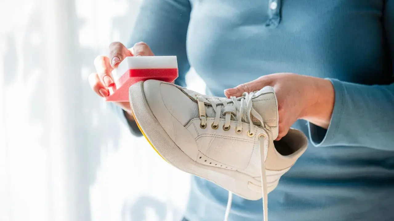 Person reinigt weiße Puma Schuhe mit einem Schwamm.