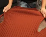Hände halten einen verfilzten und eingelaufenen Pullover aus Rippstrick. Essig als Hausmittel zur Rettung?