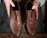 Hände präsentieren braune Lederschuhe, bereit für die Fettleder Pflege.