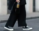 Schwarze, weite Hose und hohe Chucks kombinieren Damen für einen lässigen Look. Dazu eine schwarze Kroko-Tasche und eine Wasserflasche.