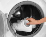 Weiße Sneaker werden in die Waschmaschine gelegt, um sie wieder sauber zu bekommen.