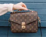 Eine Hand hält eine braune Louis Vuitton Tasche mit Monogramm-Muster. So erkennst du ein louis vuitton original.