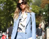 Eine Frau kombiniert einen blauen Blazer mit einem Hemd mit Vogelmotiv und auffälliger Sonnenbrille.
