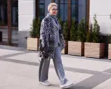 Stilvolle Frau in grauem Anzug und Strickhose, kombiniert mit einem gemusterten Mantel und Sneakern.