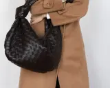 Dunkle, gewebte Tasche mit Knoten-Detail, getragen zu einem Kamelhaarmantel. Sieht aus wie eine Bottega Veneta, aber es ist ein Bottega Veneta Fake.