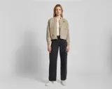 Drei Frauen präsentieren lässige Outfits. Die mittlere Frau zeigt, wie man eine Bomberjacke stylen kann, kombiniert mit weiten Jeans und Sneakern.