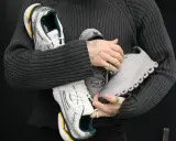 Person hält drei Paar Sneaker: weiße mit grünen Akzenten, graue und silberne. Ein Blick auf modernes shoe design.