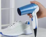 Ein weißer Sneaker mit blauen Akzenten, dessen **schuhe zu eng vorne** sind, wird mit einem blauen und weißen Föhn erwärmt.