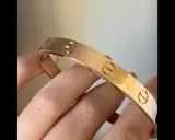 Vergleich: Fake Cartier Love Armband vs. echt. Ein glänzendes, roségoldenes Armband mit Schraubenmotiv wird von Fingern gehalten.