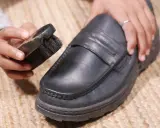 Hände reinigen einen schwarzen Lederschuh mit einer Bürste.
