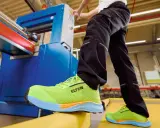 Arbeiter in leuchtend grünen Sicherheitsschuhen von ELTEN an einer Maschine. Seit wann gibt es Schuhe? Schon seit der Steinzeit, um die Füße zu schützen.