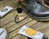 Schwarze Lederstiefel werden mit Tapir Lederpflegecreme und Bürsten gepflegt.