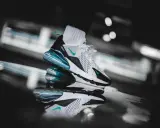 Ein stylischer Nike Air Max 270 in Weiß mit türkisen Akzenten, der auf einer spiegelnden Oberfläche steht. Ein zeitloser Klassiker unter den Nike Air Max alte Modelle.