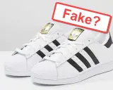 Weiße Adidas Sneaker mit schwarzen Streifen und goldenem Logo. Ein rotes Schild fragt: "Fake?". So kannst du Adidas Fake erkennen.