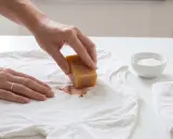Hand reibt mit Seifenstück über Blutfleck auf weißem T-Shirt, um gewaschene Blutflecken entfernen zu können.