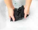 Hände waschen ein schwarzes Seidentuch in schaumigem Wasser. Sanfte Pflege für empfindliche Stoffe.
