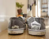 Graue Sneaker mit Teebeuteln, die aus den Fersen ragen. Ein ungewöhnlicher Trick, um Gerüche zu bekämpfen.