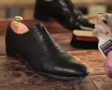 Schuhe polieren: Ein schwarzer Lederschuh mit Schuhspanner wird mit einem Tuch und Saphir Reno'Mat gereinigt.