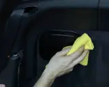 Hand wischt mit gelbem Tuch über schwarzes Kunstleder im Auto. So einfach ist Kunstleder reinigen.