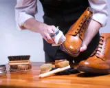 Mann poliert braune Glattleder-Schuhe mit einem Tuch. Pflege für Glattleder ist wichtig.
