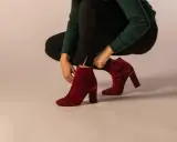 Eine Frau zieht rote Wildleder-Stiefeletten an. Verschiedene lederarten schuhe sind hier zu sehen, wie diese eleganten Damenschuhe.