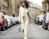 Eine Frau in einem eleganten beigen Hosenanzug mit passendem Westchen und Blazer spaziert durch eine Pariser Straße. Die weiten Hosen und die lässige Silhouette der Schuhe zu Hosenanzug Damen sind perfekt für einen stilvollen Auftritt.