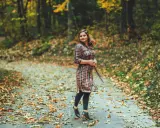 Frau im karierten Kleid mit Leggings steht auf einem herbstlich bedeckten Weg.