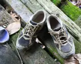 Schuhe stinken was tun? Diese schmutzigen Wanderschuhe liegen auf moosbewachsenen Baumstämmen.