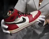 Ein Paar rote und weiße Air Jordan 1 Sneaker, die als die teuersten Schuhe der Welt gelten, werden von Händen in weißen Handschuhen gehalten.