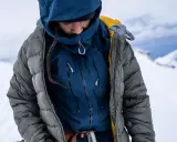 Person in Daunenjacke im Schnee. Die Jacke ist grau, darunter eine blaue Schicht. Perfekt für das Daunenjacke waschen nach der Tour.