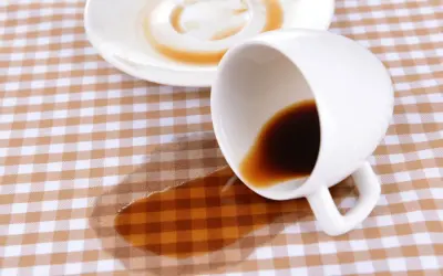 Um Kaffeeflecken zu entfernen, ist hier ein umgekippter Becher mit Kaffee auf kariertem Stoff.
